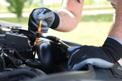 Photo of Worker checking motor oil level in car with dipstick, closeup