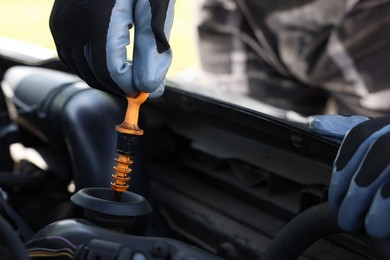 Photo of Worker checking motor oil level in car with dipstick, closeup