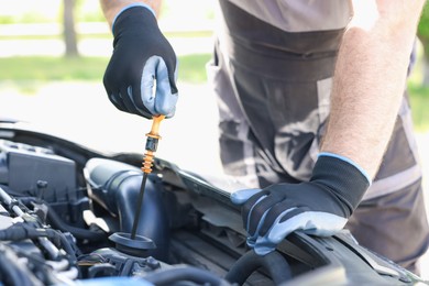 Photo of Worker checking motor oil level in car with dipstick, closeup