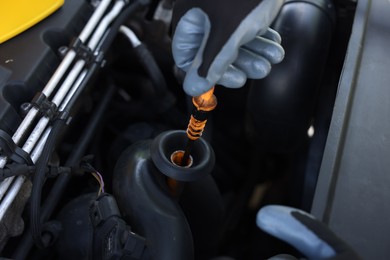 Photo of Worker checking motor oil level in car with dipstick, closeup