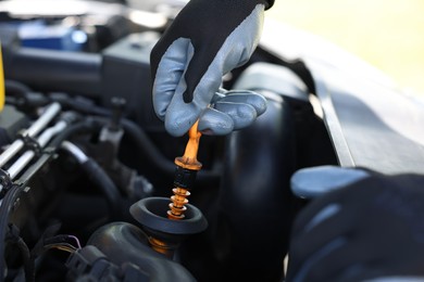 Photo of Worker checking motor oil level in car with dipstick, closeup