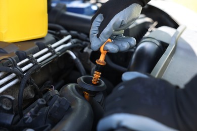 Photo of Worker checking motor oil level in car with dipstick, closeup