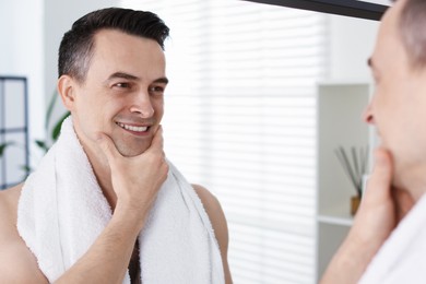 Photo of Smiling man after shaving looking at mirror in bathroom
