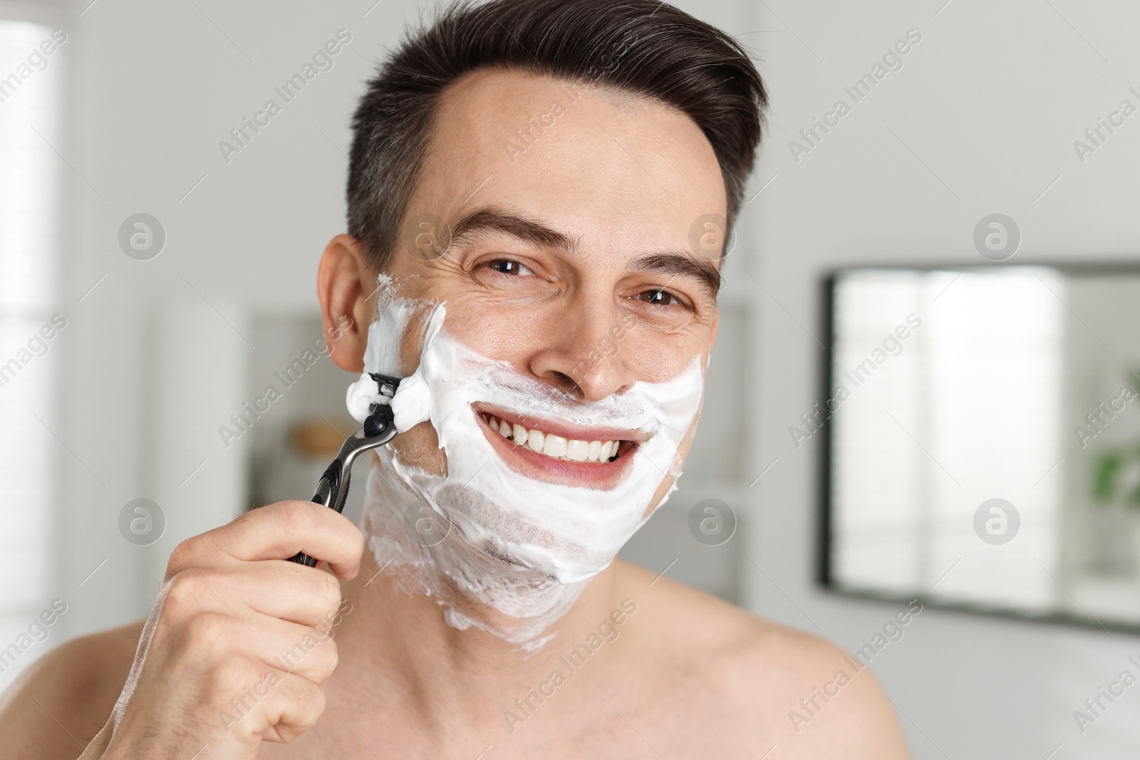 Photo of Smiling man shaving with razor at home