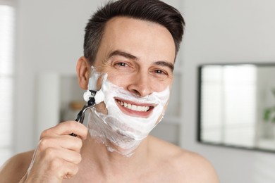Photo of Smiling man shaving with razor at home