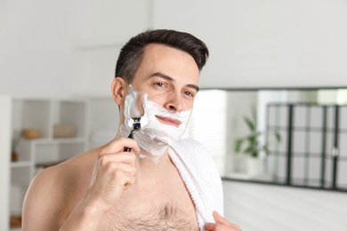 Photo of Handsome man shaving with razor at home
