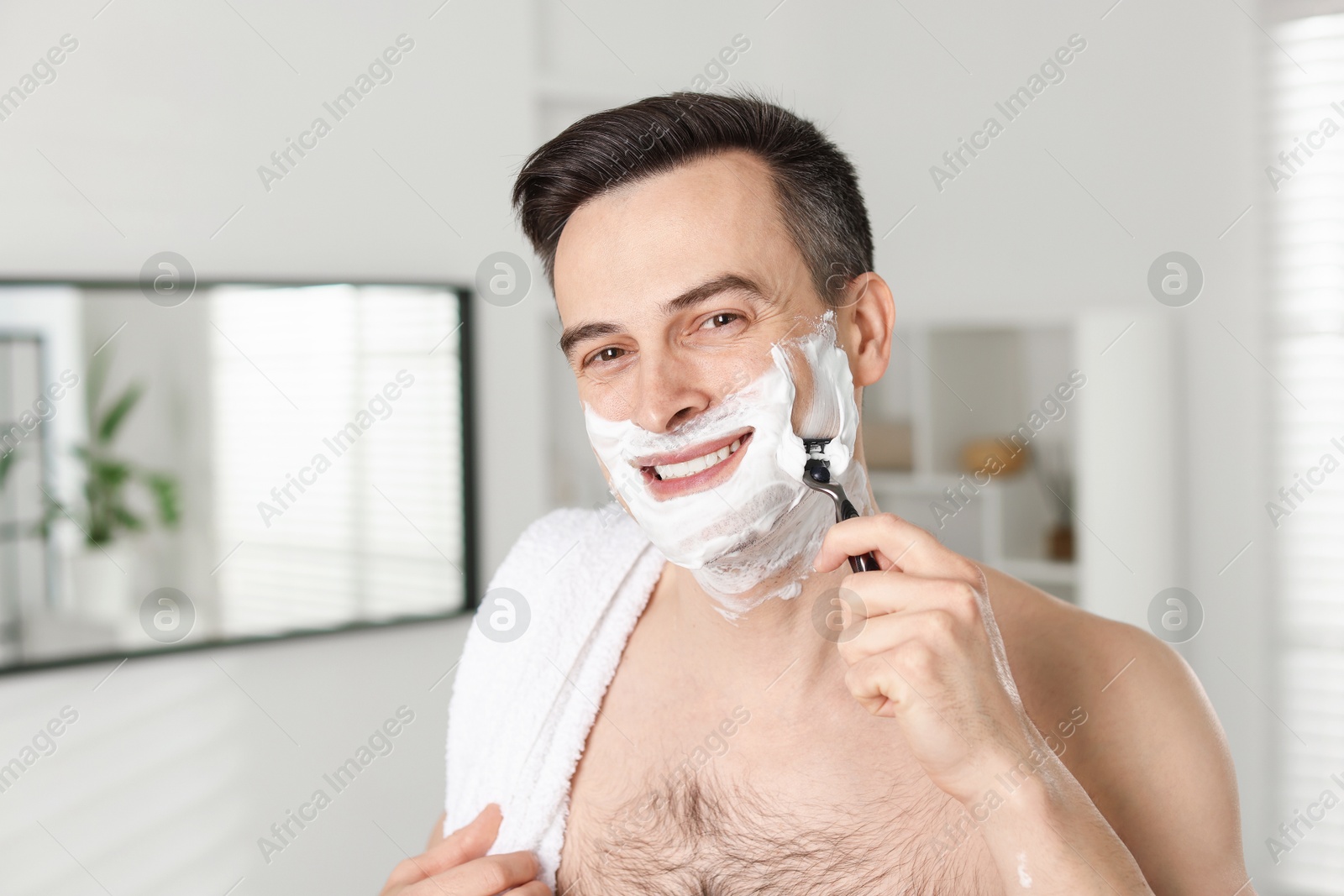 Smiling man shaving with razor at home Photo of Smiling man shaving with razor at home