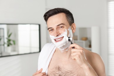 Photo of Smiling man shaving with razor at home