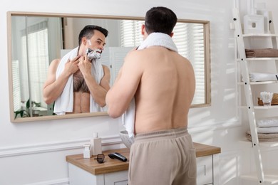 Photo of Handsome man shaving with razor near mirror at home