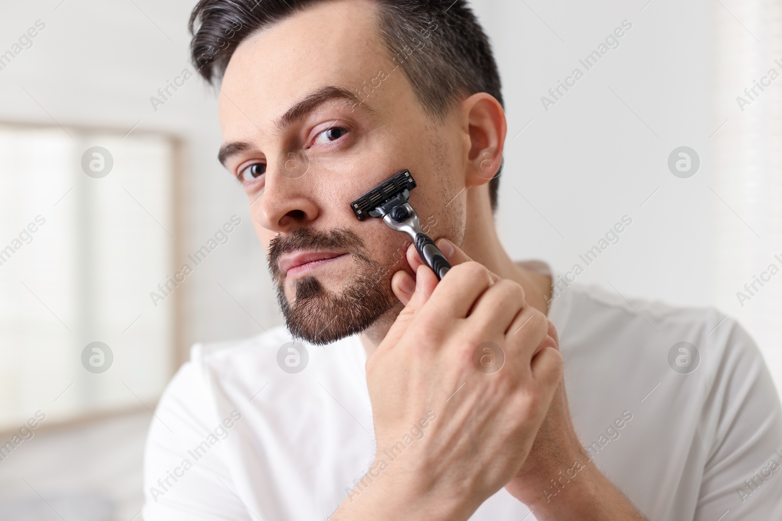 Photo of Handsome man shaving with razor at home, closeup