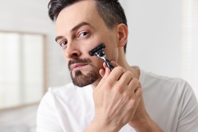 Photo of Handsome man shaving with razor at home, closeup