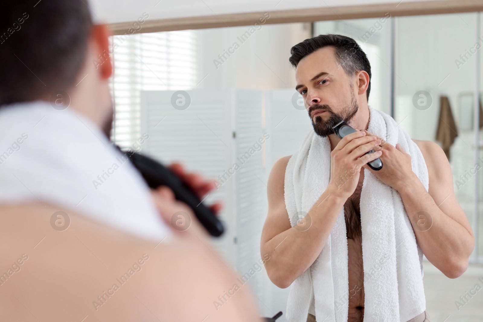 Handsome man shaving with trimmer near mirror in bathroom Photo of Handsome man shaving with trimmer near mirror in bathroom