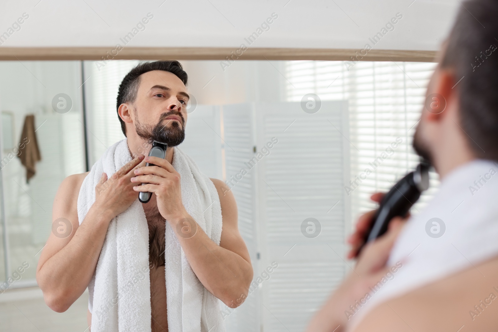 Handsome man shaving with trimmer near mirror in bathroom Photo of Handsome man shaving with trimmer near mirror in bathroom