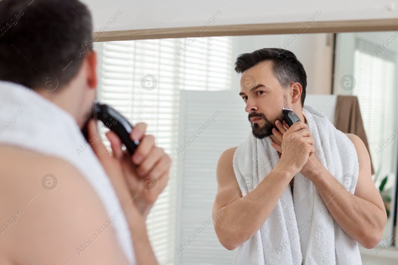 Handsome man shaving with trimmer near mirror in bathroom Photo of Handsome man shaving with trimmer near mirror in bathroom