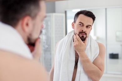 Photo of Handsome man before shaving looking at mirror in bathroom