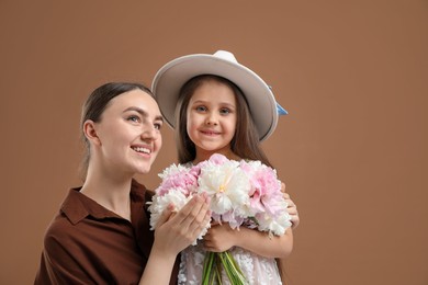 Photo of Mother and her daughter with bouquet of beautiful peonies on brown background, space for text