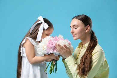 Photo of Cute little girl giving her mother bouquet of beautiful peonies on light blue background