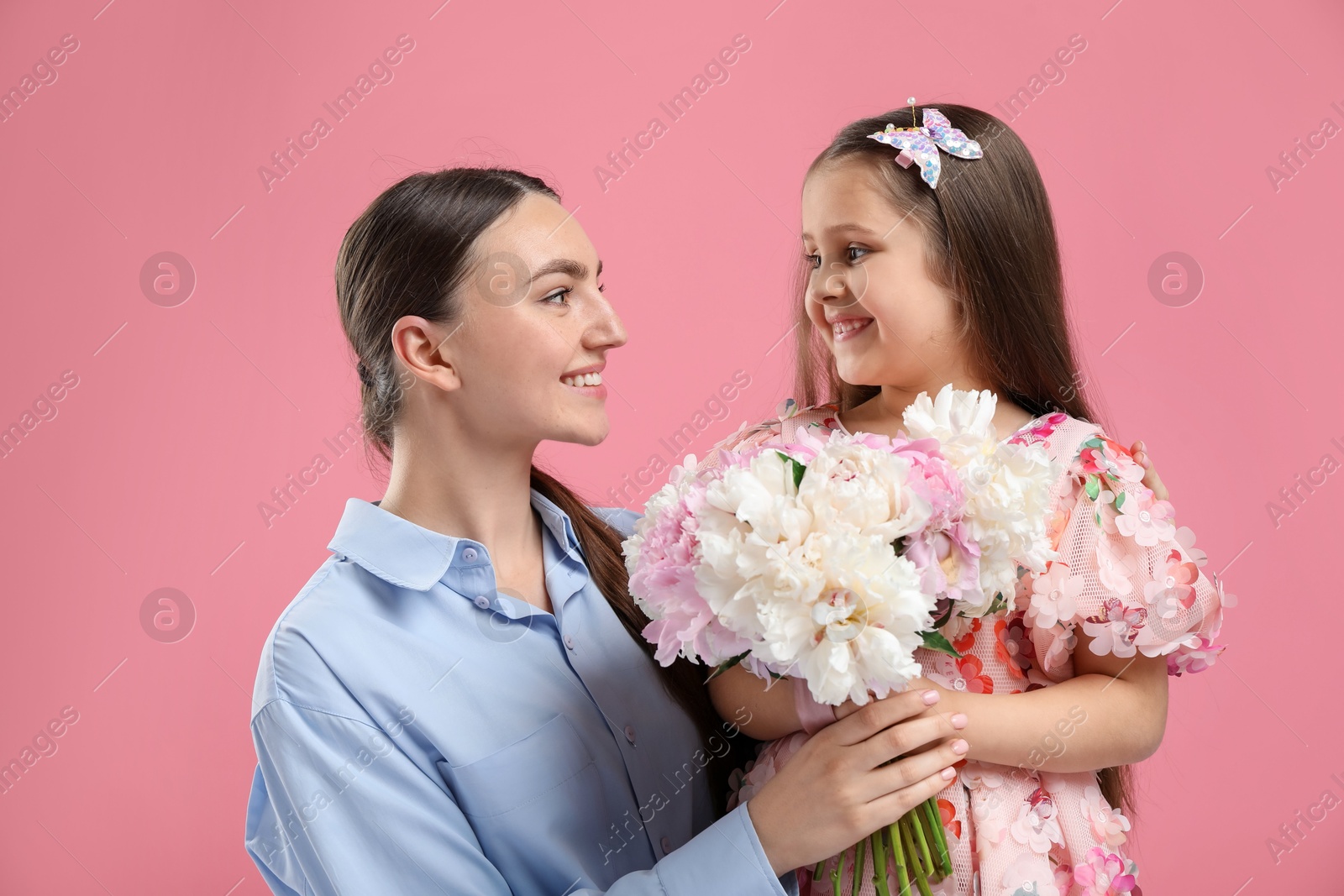 Mother and her daughter with bouquet of beautiful peonies on pink background Photo of Mother and her daughter with bouquet of beautiful peonies on pink background
