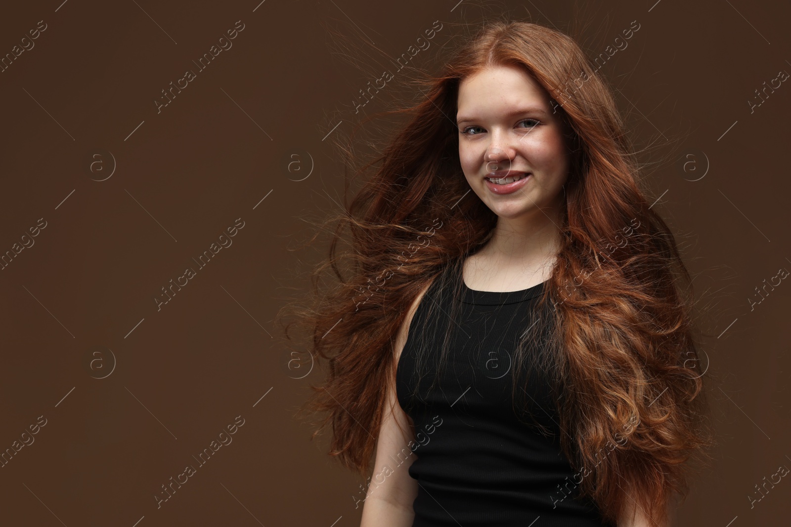 Portrait of smiling teenage girl with healthy wavy hair on brown background. Space for text Photo of Portrait of smiling teenage girl with healthy wavy hair on brown background. Space for text
