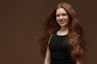 Photo of Portrait of smiling teenage girl with healthy wavy hair on brown background. Space for text