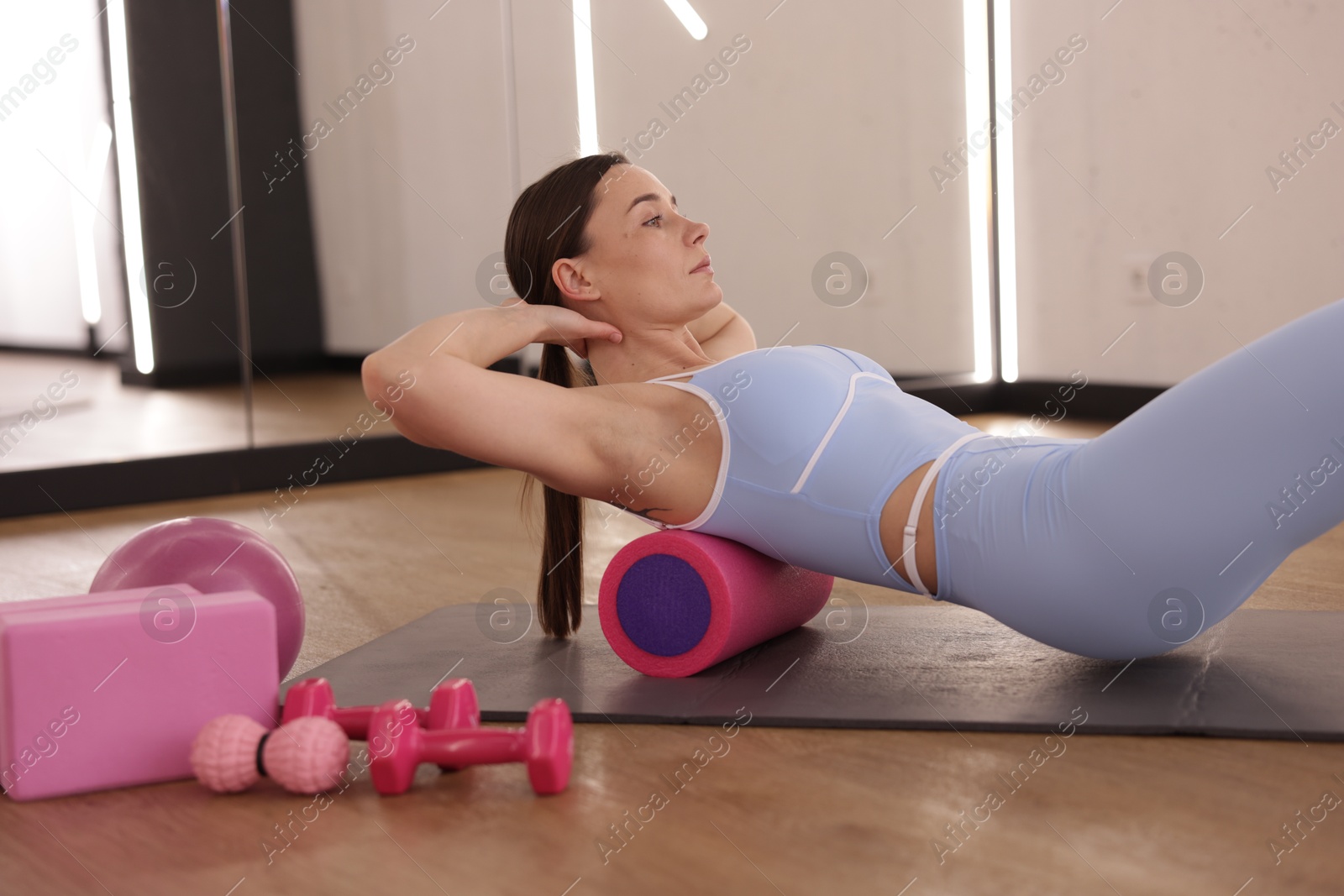Woman exercising with foam roller on mat in fitness studio Photo of Woman exercising with foam roller on mat in fitness studio