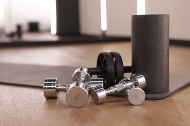 Photo of Dumbbells, ab roller and mat on floor in fitness studio
