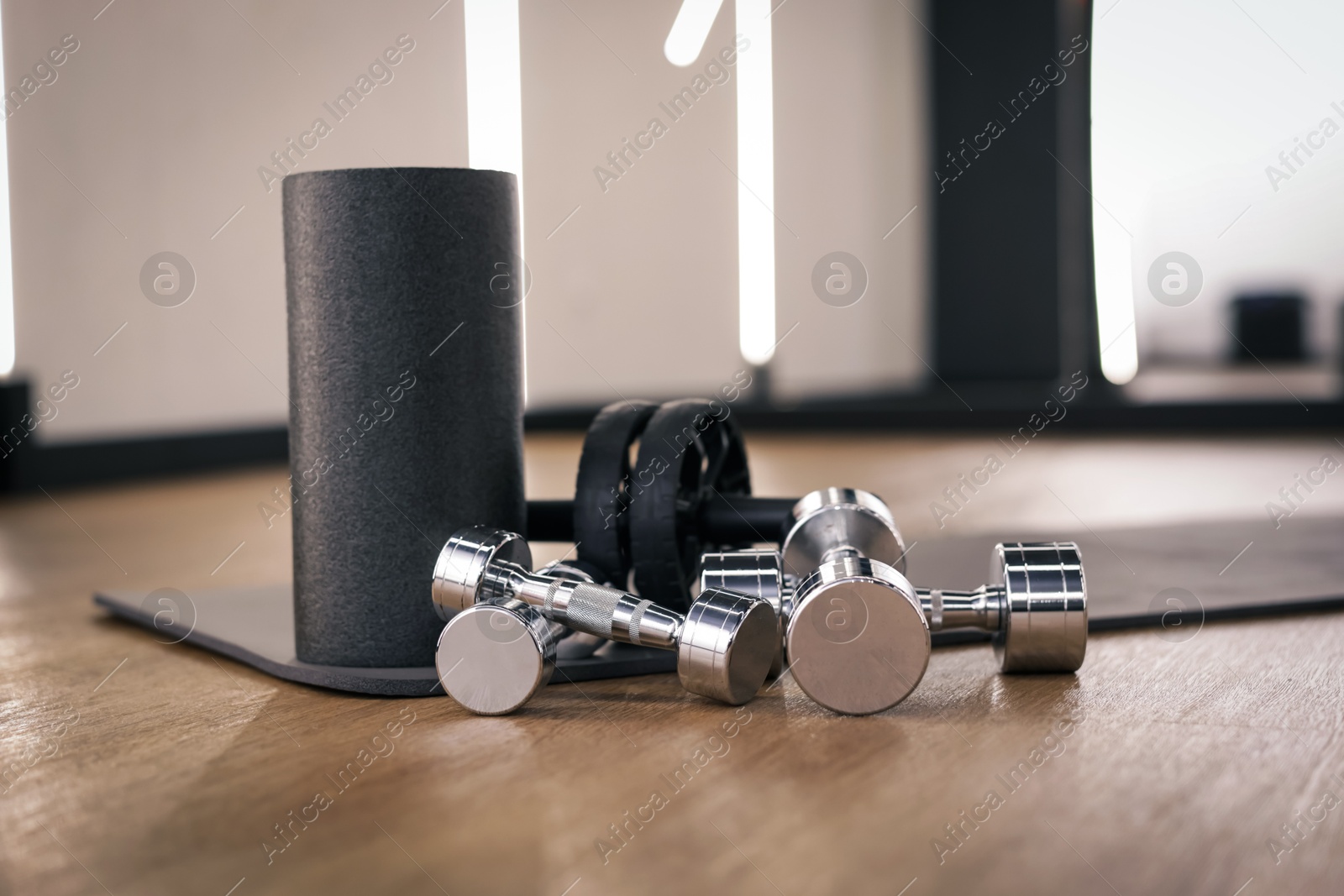 Dumbbells, ab roller and mat on floor in fitness studio Photo of Dumbbells, ab roller and mat on floor in fitness studio