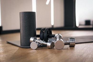 Photo of Dumbbells, ab roller and mat on floor in fitness studio