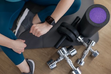 Photo of Woman checking fitness tracker during training indoors, top view