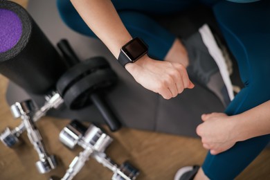 Photo of Woman checking fitness tracker during training indoors, top view