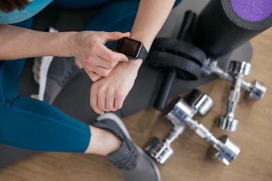 Photo of Woman checking fitness tracker during training indoors, top view