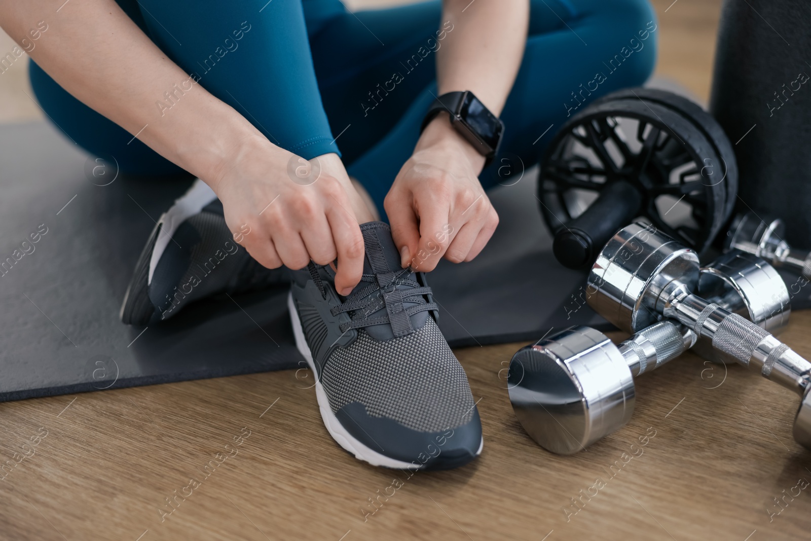Woman tying shoelaces on floor in fitness studio, closeup Photo of Woman tying shoelaces on floor in fitness studio, closeup