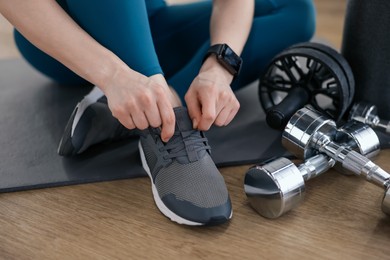Photo of Woman tying shoelaces on floor in fitness studio, closeup