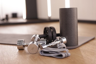 Photo of Dumbbells, elastic band, foam roller and mat on floor in fitness studio, closeup