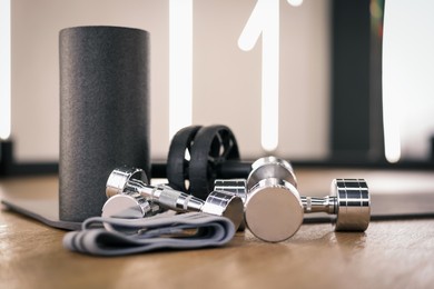 Photo of Dumbbells, elastic band, foam roller and mat on floor in fitness studio, closeup