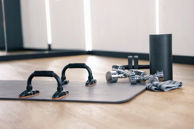 Photo of Push up bars, dumbbells, foam roller and elastic band on floor in fitness studio