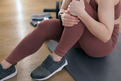 Photo of Sportswoman with leg injury suffering from knee pain in fitness studio, closeup