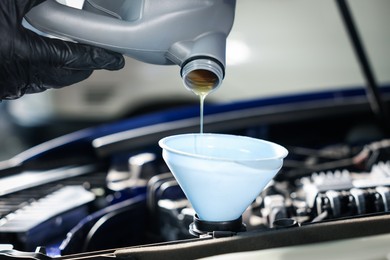 Photo of Worker pouring motor oil from canister into car engine, closeup