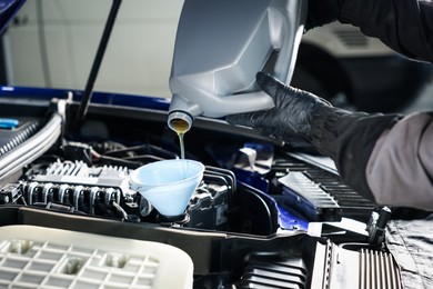 Photo of Worker pouring motor oil from canister into car engine, closeup