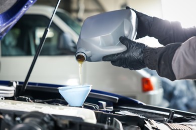 Photo of Worker pouring motor oil from canister into car engine, closeup