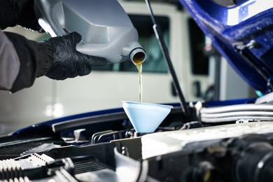 Photo of Worker pouring motor oil from canister into car engine, closeup