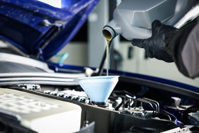 Photo of Worker pouring motor oil from canister into car engine, closeup