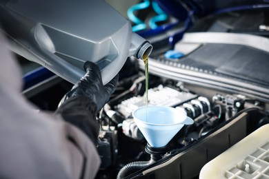 Photo of Worker pouring motor oil from canister into car engine, closeup