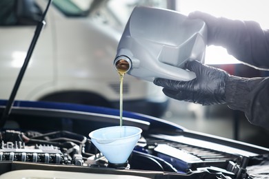 Photo of Worker pouring motor oil from canister into car engine, closeup