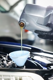 Photo of Worker pouring motor oil from canister into car engine, closeup