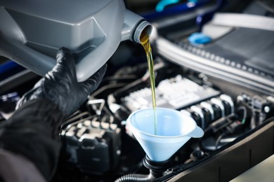 Photo of Worker pouring motor oil from canister into car engine, closeup