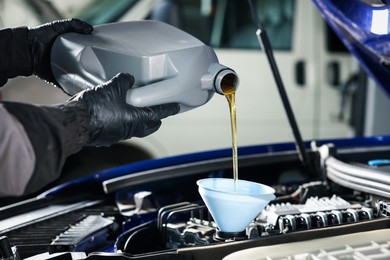 Photo of Worker pouring motor oil from canister into car engine, closeup