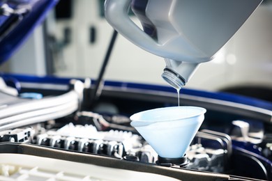 Photo of Pouring motor oil from bottle into car engine, closeup
