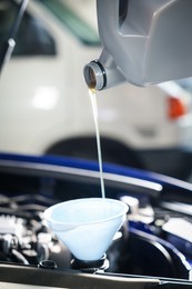Photo of Pouring motor oil from bottle into car engine, closeup