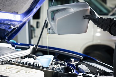 Photo of Worker pouring motor oil from canister into car engine, closeup